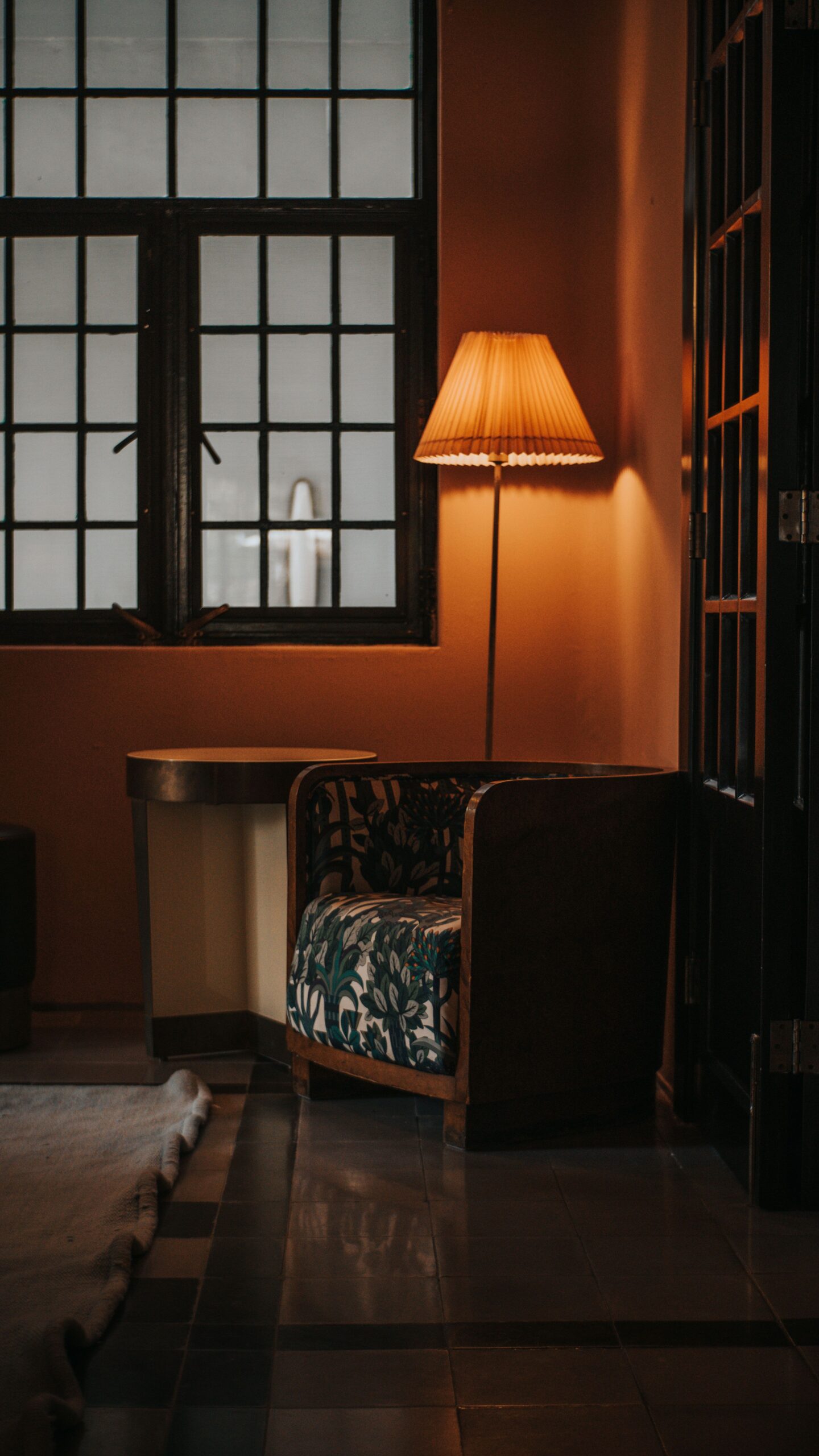 Armchair and floor lamp in a warm interior with natural light and dark window frames